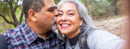 A mature with a beard kisses the cheek of his wife, who has long gray hair