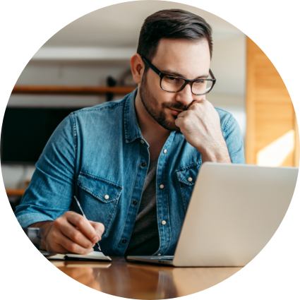 Man with glasses on takes notes while looking at laptop screen