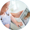 Circle image of child being held looking at computer