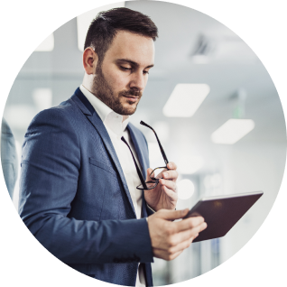 Man in suit holds his glasses in his hand while looking down at tablet