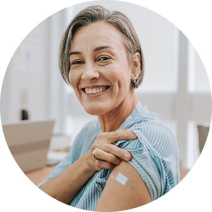 A white woman sitting in an office smiles as she lifts up her sleeve, revealing a bandage on her arm.