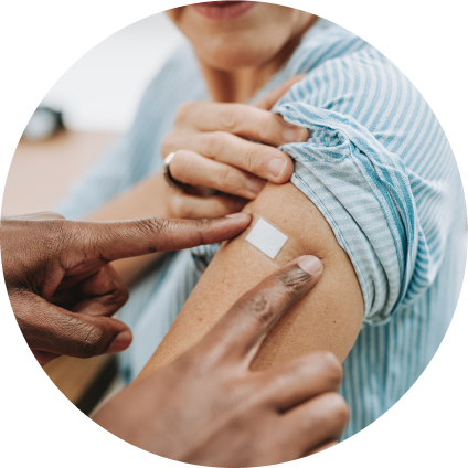 A Black health care worker puts a band-aid on the upper arm of a white person holding up their sleeve after a vaccine.