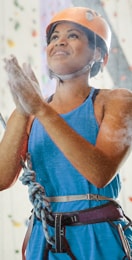 Athletic woman in a rock climbing safety helmet and harness dusting her hands in preparation to climb an indoor climbing wall