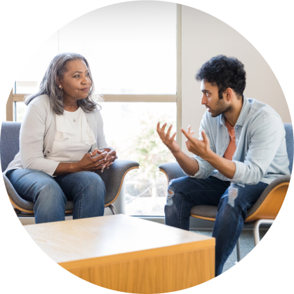 A therapist, a middle-aged Black woman, sits across from a young man with dark hair as he explains something.