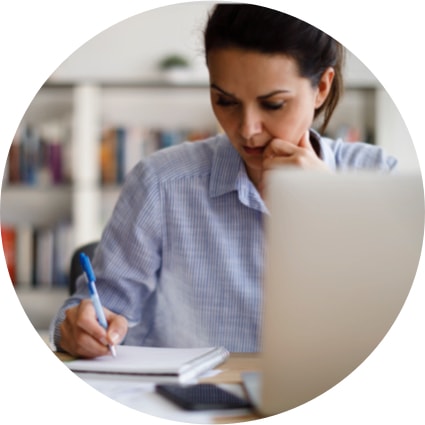 Woman making notes on a notepad while working on her laptop