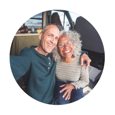 A smiling, balding man and a smiling woman with mid-length gray hear squeezing together to take a sitting selfie