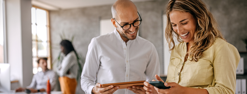 Two coworkers smiling and looking at mobile devices