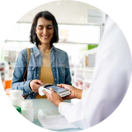 A white woman with dark hair and a blue denim shirt smiles as she checks out at the pharmacy.